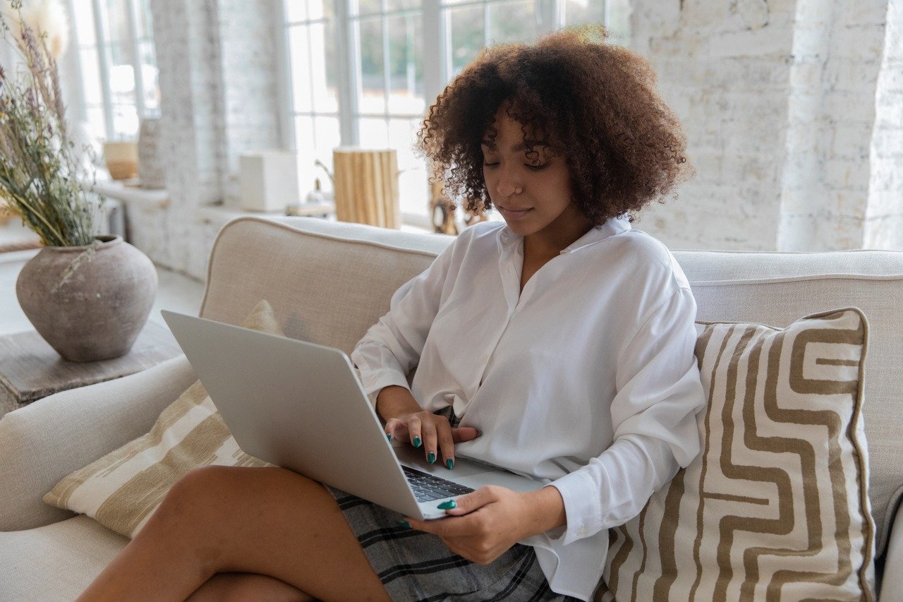 mulher usando um laptop e sentada em um sofá