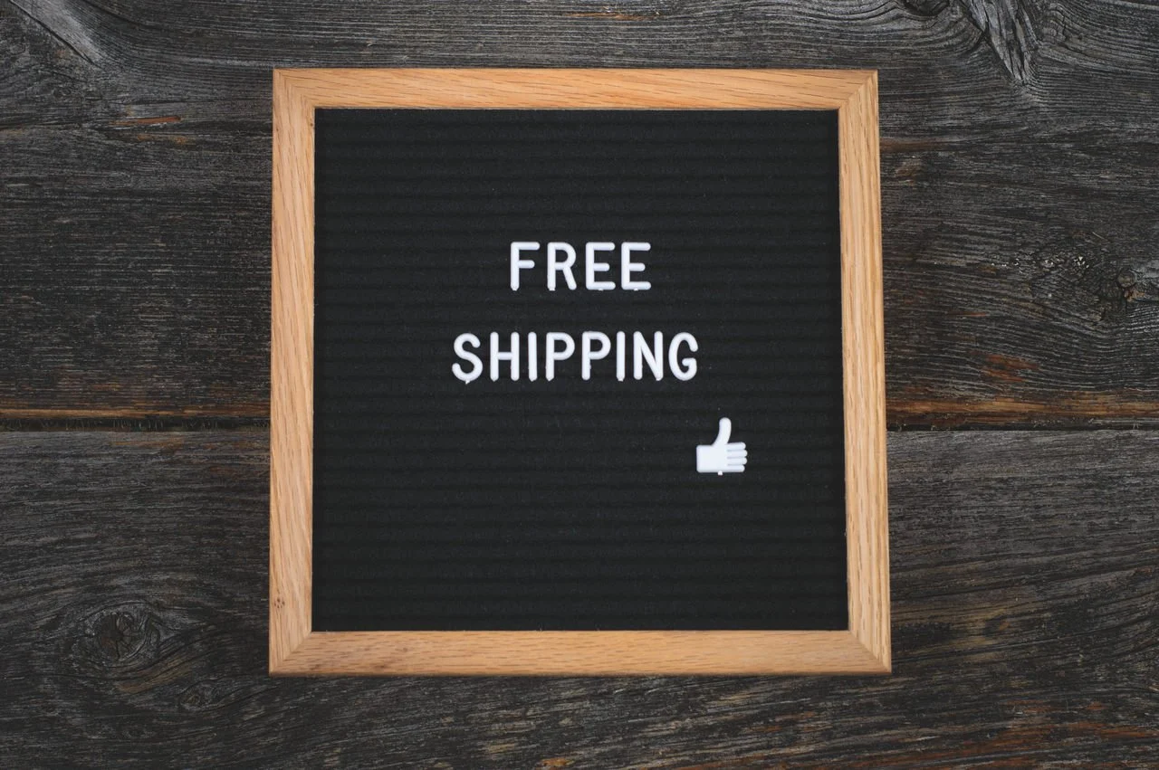 "Free shipping" written on a wooden sign on a dark wooden table