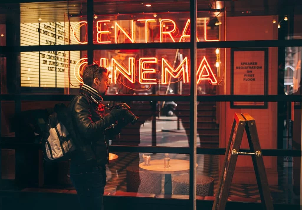 fotografer berdiri di depan gedung dengan tulisan neon