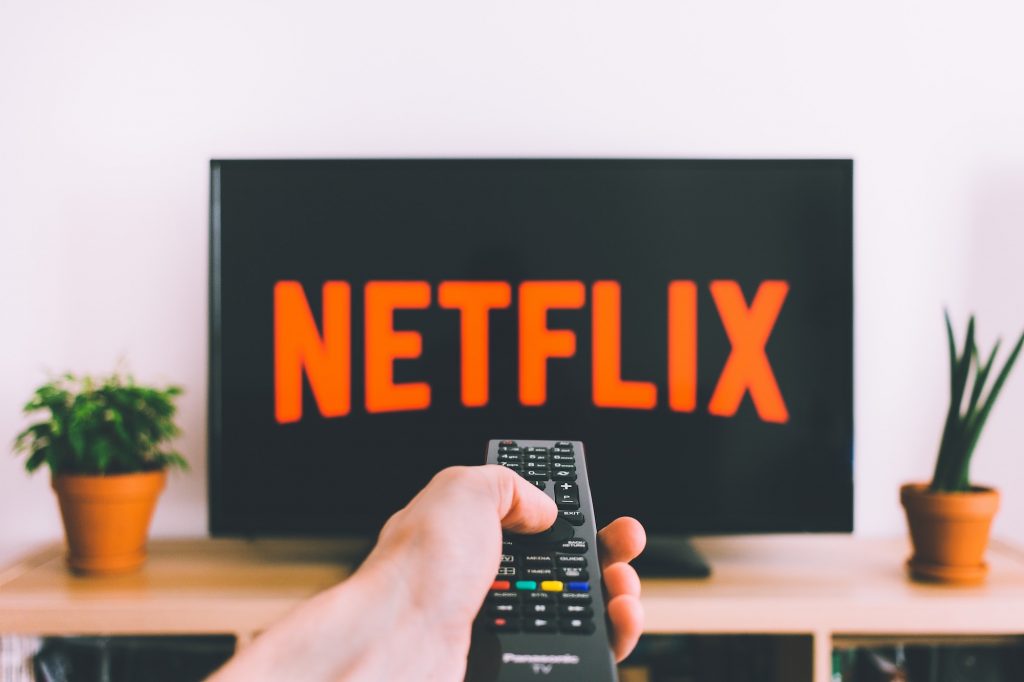 Netflix 화면 앞에서 TV 리모컨을 들고 있는 손