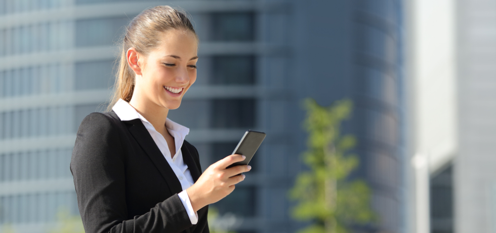 Bella donna con un telefono cellulare in strada che legge un messaggio di testo con edifici per uffici sullo sfondo