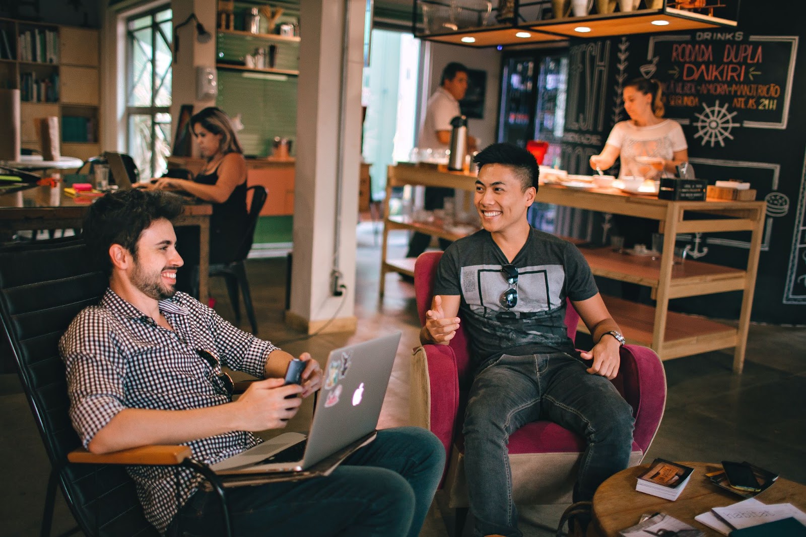 Two men in a cafe working on their laptops and laughing.