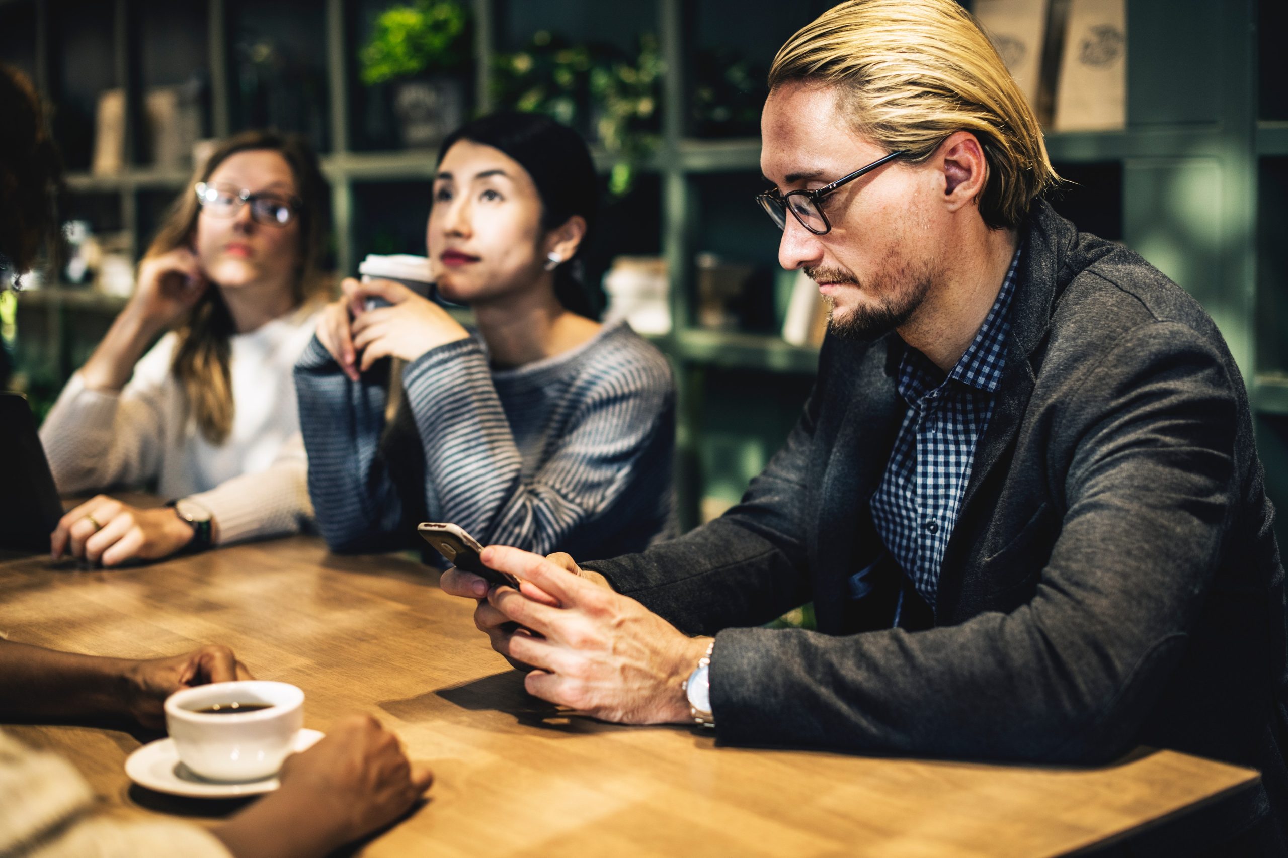 Hombre sentado con su teléfono en un café junto a otras personas