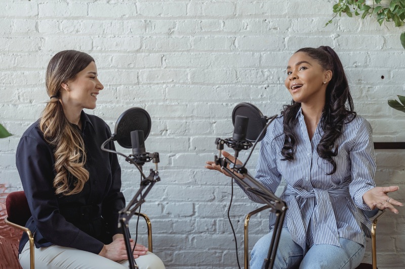 Dos mujeres frente a micrófonos grabando juntas un podcast