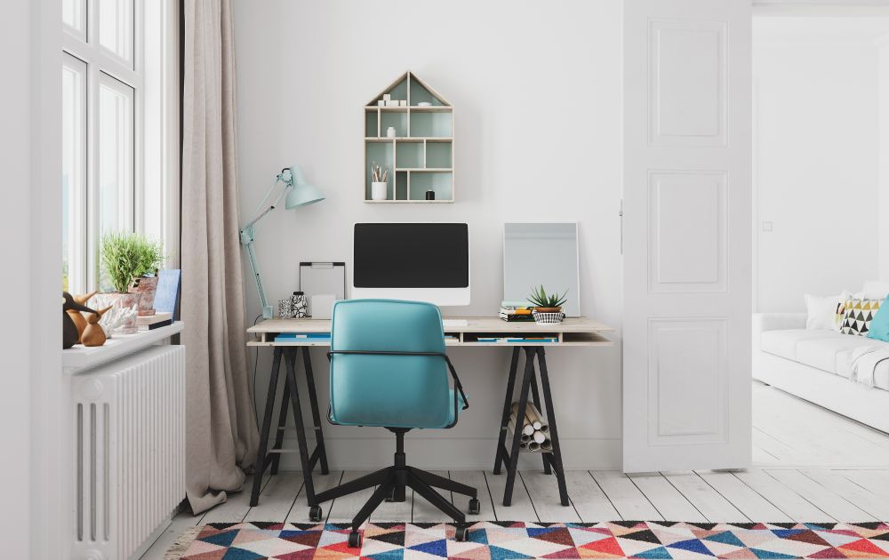 Home office con sedia girevole blu, scrivania in legno e ferro, pareti bianche, tende bianco sporco, moquette colorata e accenti