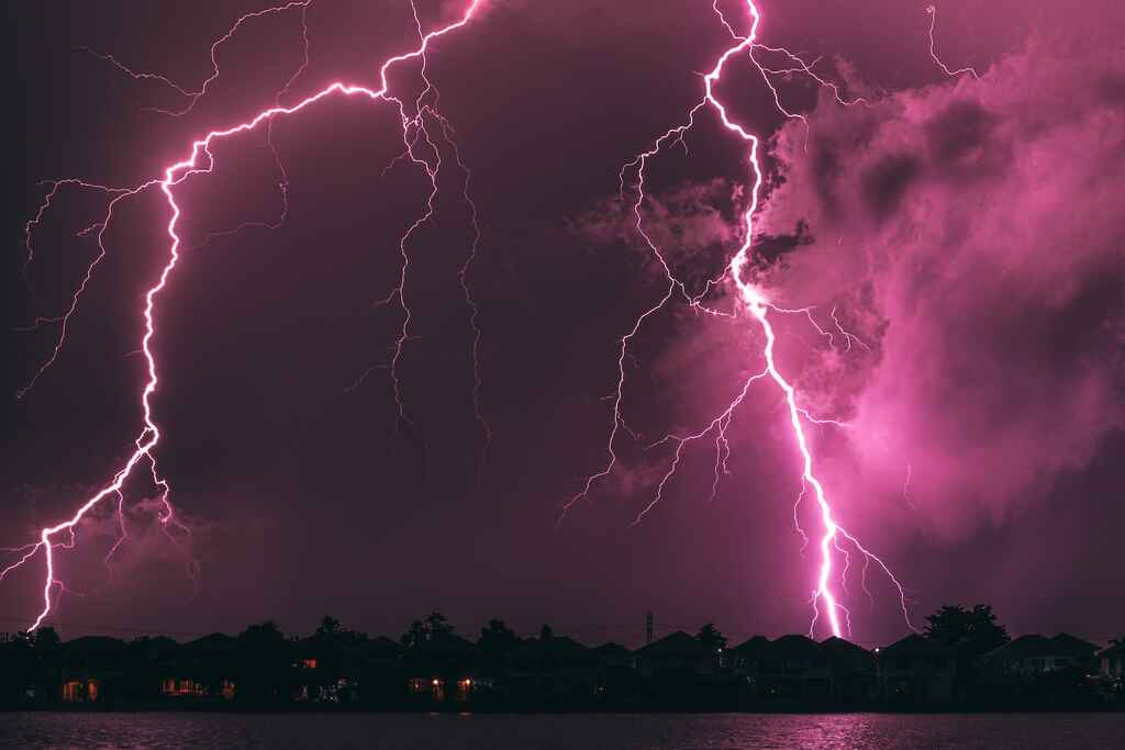 Foto dua sambaran petir besar di atas kota kecil. Langit menyala merah jambu