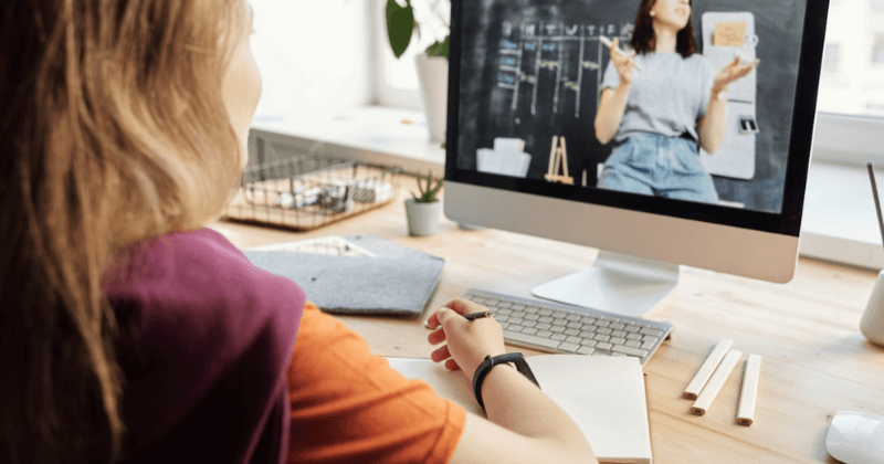 Mujer tomando notas viendo un curso de formación en la computadora.