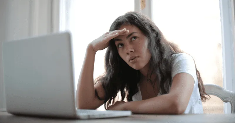 Mulher com olhar preocupado trabalhando no laptop.