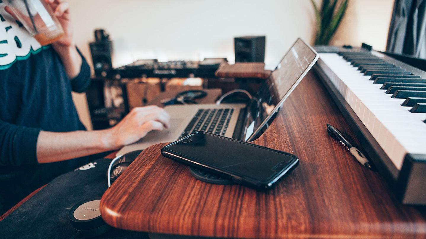 Persona seduta al proprio laptop, con la tastiera di un pianoforte e il telefono sulla scrivania.