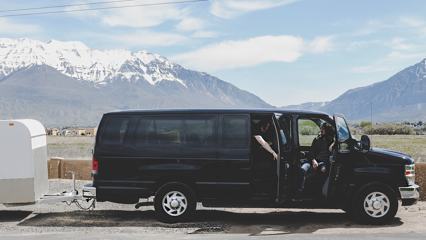 トレーラー付きの黒いバンが、遠くに山を望む道端に駐車されています