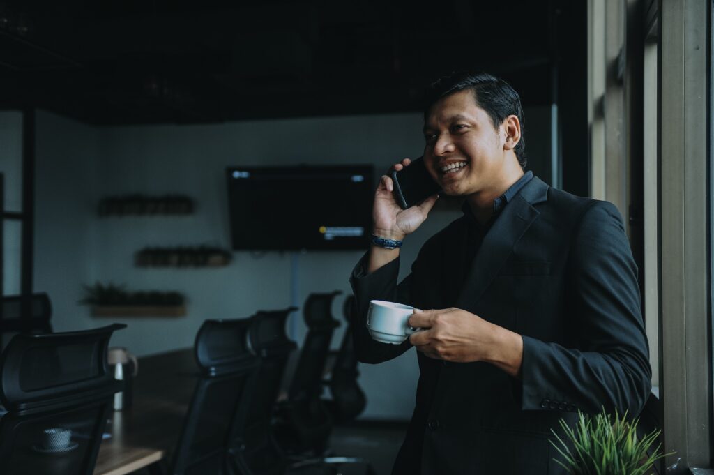 Um executivo de negócios e uma pessoa negra conversam ao telefone celular em uma sala de conferências vazia durante um intervalo para o café para ilustrar táticas de marketing baseadas em contas.