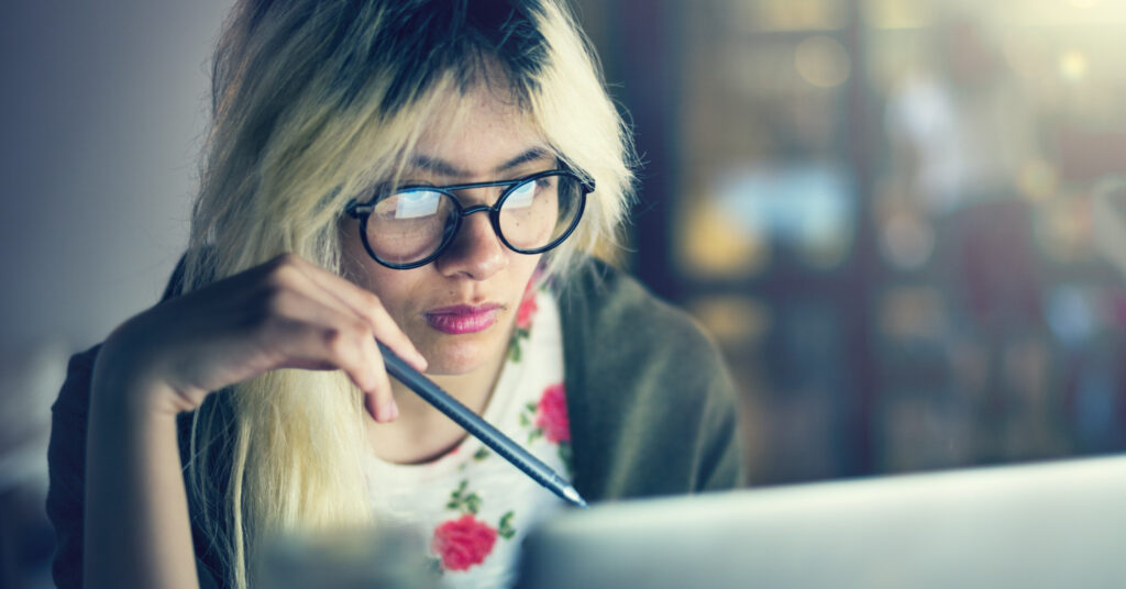 Une jeune femme avec un stylo regarde un ordinateur portable et réfléchit à sa FAQ SEO