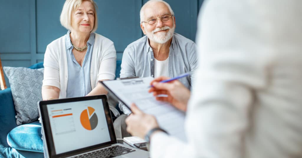 Deux seniors attirés par le marketing automation rencontrent leur gestionnaire de fortune, qui prend des notes au premier plan.