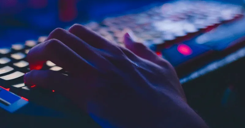 Una mano escribe en un teclado en una habitación oscura.