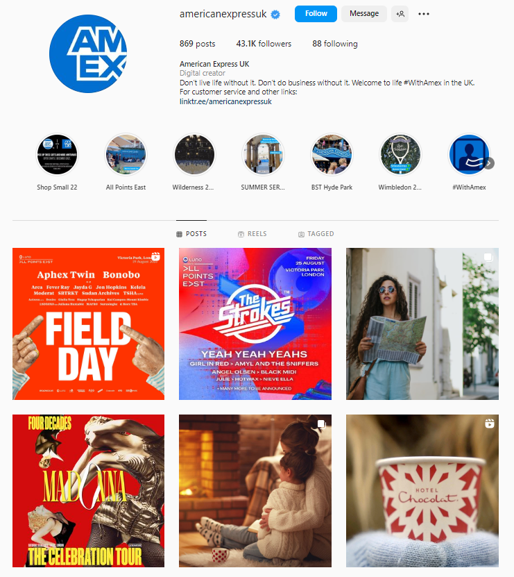 A bold collection of colours. In typical Instagram layout, the AmEx logo is in blue in the top left, and next to it are details about the company and how many posts/followers/following they have. 

Beneath that is a row of smaller circles which contain brief snippets of videos and information. 

Beneath that are six brightly coloured posts advertising various events like The Strokes, Field Day, and Madonna, as well as brand deals with Hotel Chocolat, a picture of a woman in sunglasses holding a map, and another picture of a couple in white jumpers snuggled up by an open fire. 