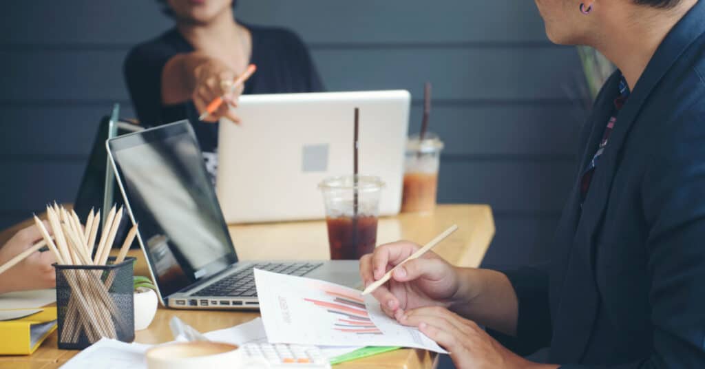 gros plan d'une table de conférence occupée avec un collègue pointant vers une fiche technique pour illustrer l'idée des meilleures pratiques d'aide à la vente