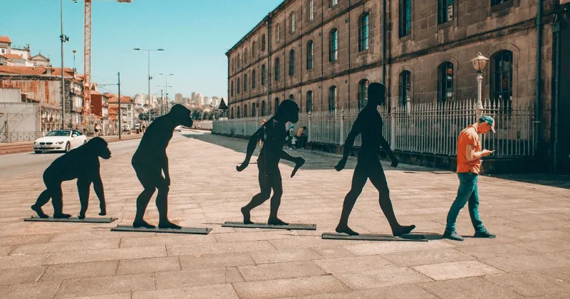 Statue di primati che si evolvono in un essere umano in piedi che guarda il telefono.