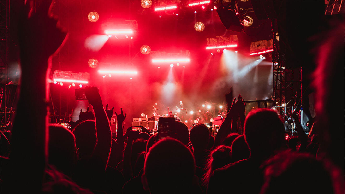 Blog Bandzoogle: cum să fii rezervat la festivaluri de muzică. Imaginea unei mulțimi care urmărește o trupă cântând pe o scenă a unui festival noaptea, vedere din mulțimea de oameni.