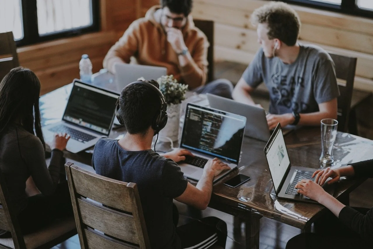 pessoas que trabalham em um espaço de trabalho com seus laptops e fones de ouvido