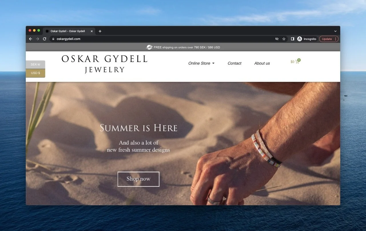 une main portant des bracelets Oskar Gydell touchant le sable